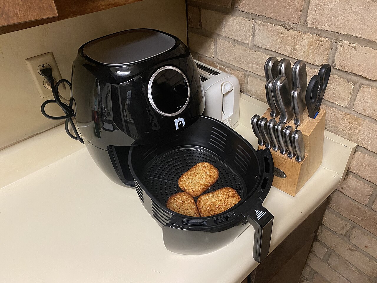 A black air fryer with its basket pulled out, showing food inside, on a kitchen counter