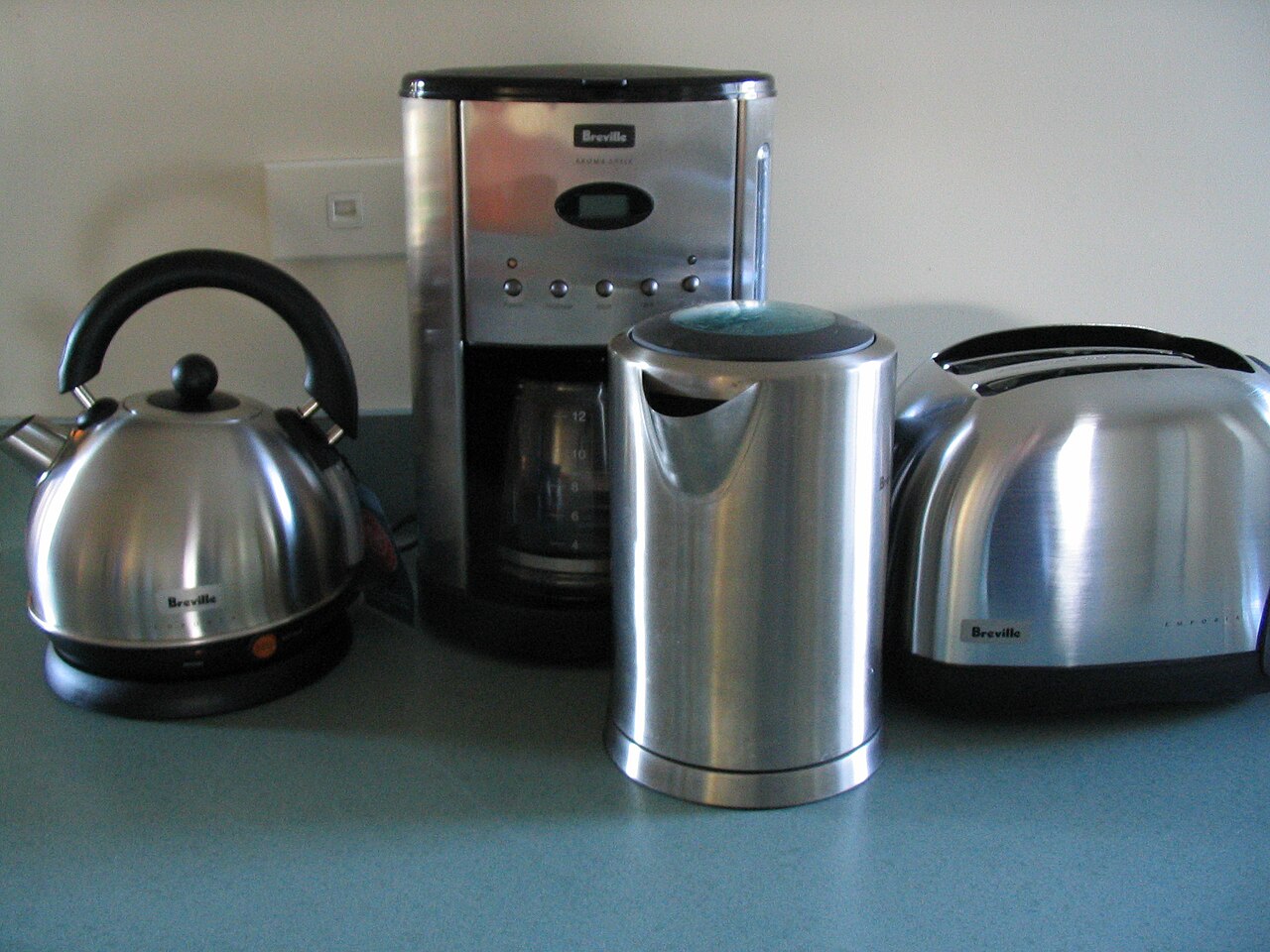 Breville stainless-steel kitchen appliances on a counter, including an earlier two-slice Breville toaster at right